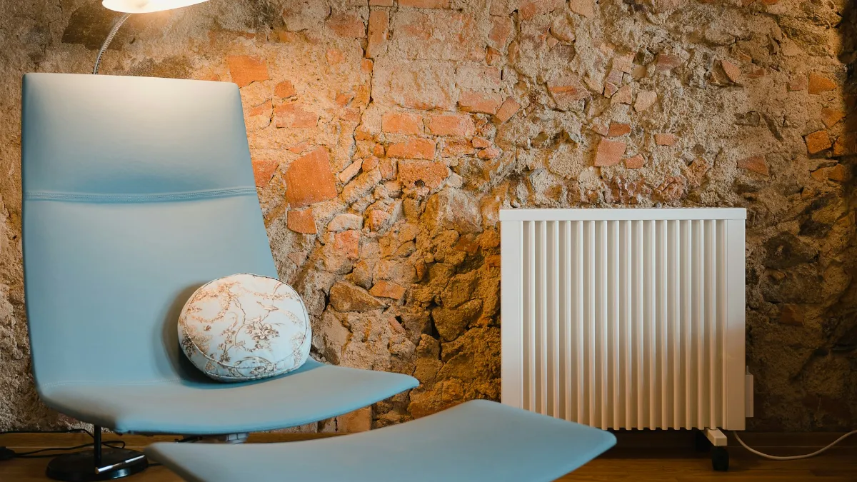 Radiateur électrique blanc dans un salon au mur de pierre, à côté d’un fauteuil design