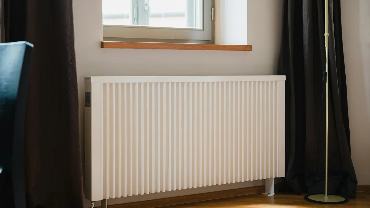 Radiateur électrique blanc installé sous une fenêtre, entre deux rideaux sombres
