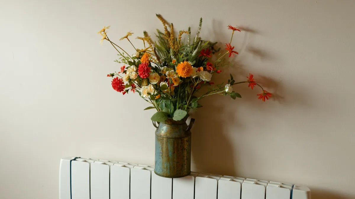 Bouquet de fleurs dans un vase posé au-dessus d’un radiateur blanc contre un mur clair